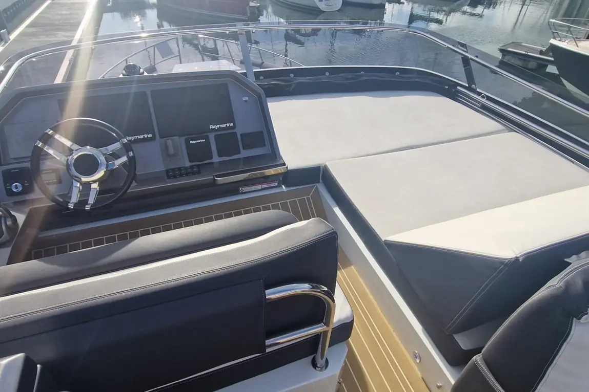 Modern boat cockpit featuring a Raymarine display and a sleek steering wheel, with plush seating and deck view of docked boats.